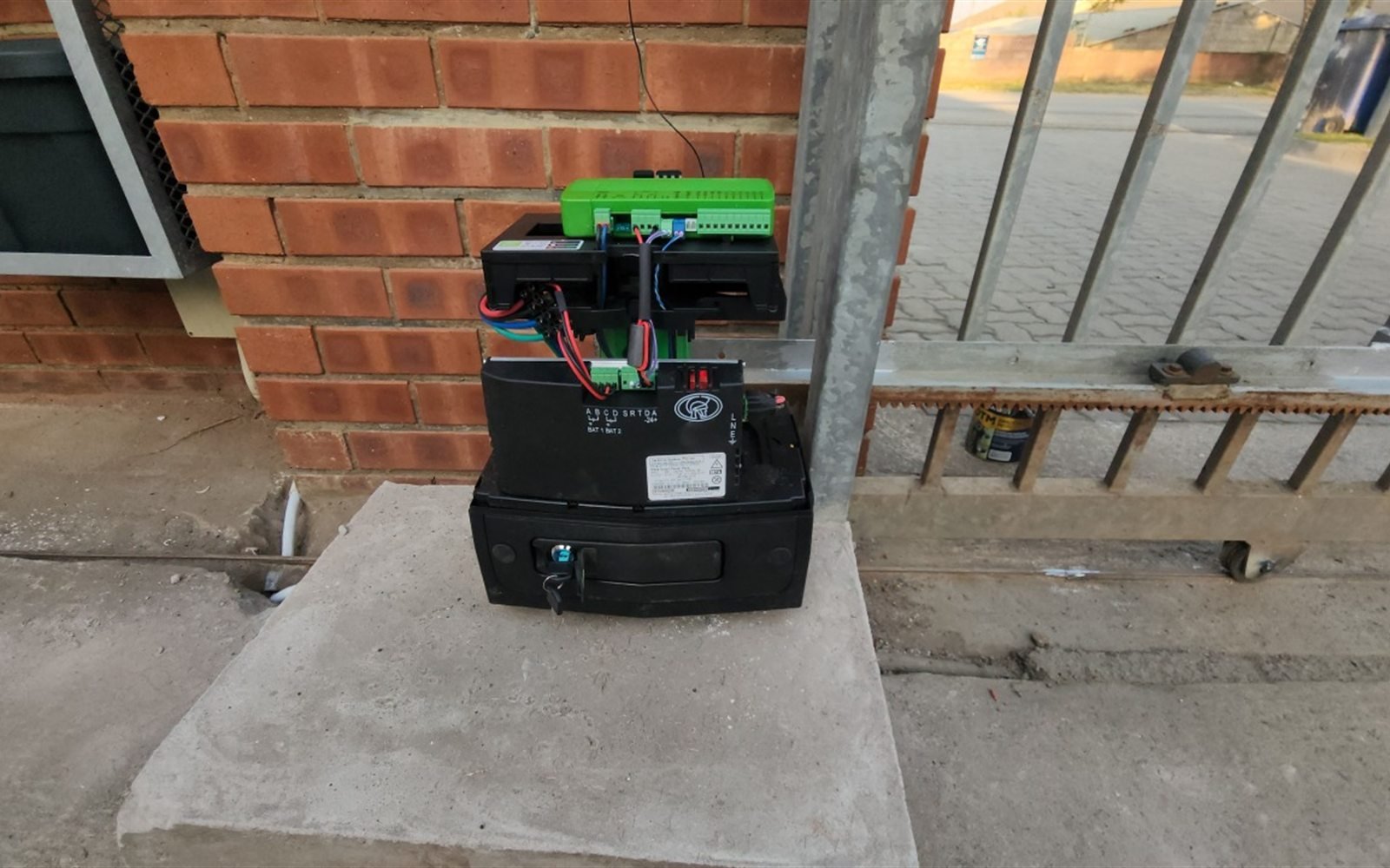 Green sliding gate motor and backup battery fitted to a brick pillar