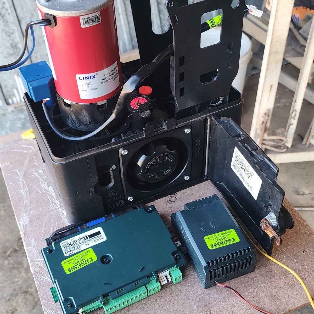 Sliding gate motor opened on a workbench with its control board and capacitor exposed during refurbishment