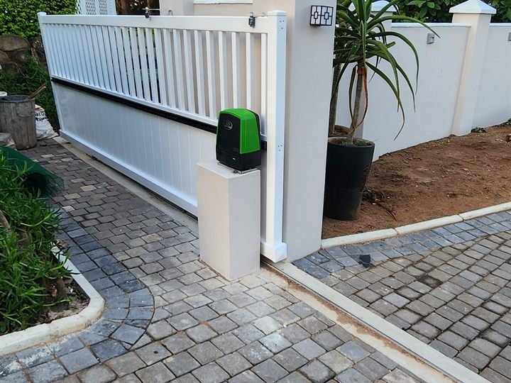 White sliding driveway gate between matching pillars with a green gate motor