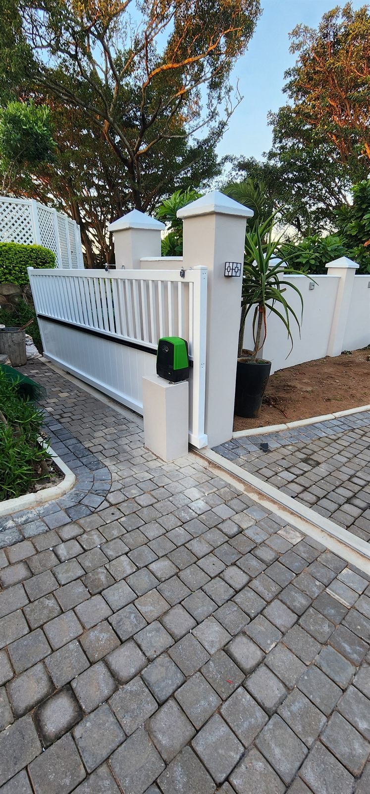 White sliding driveway gate between matching pillars with a green gate motor